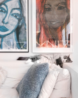 Two art posters portraying women and a cat sleeping on top of sofa